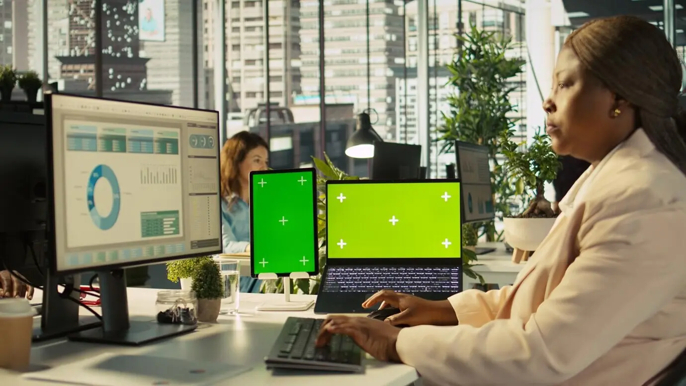 Изолированные устройства с экранами на офисном столе рядом с сотрудником, редактирующим документы.